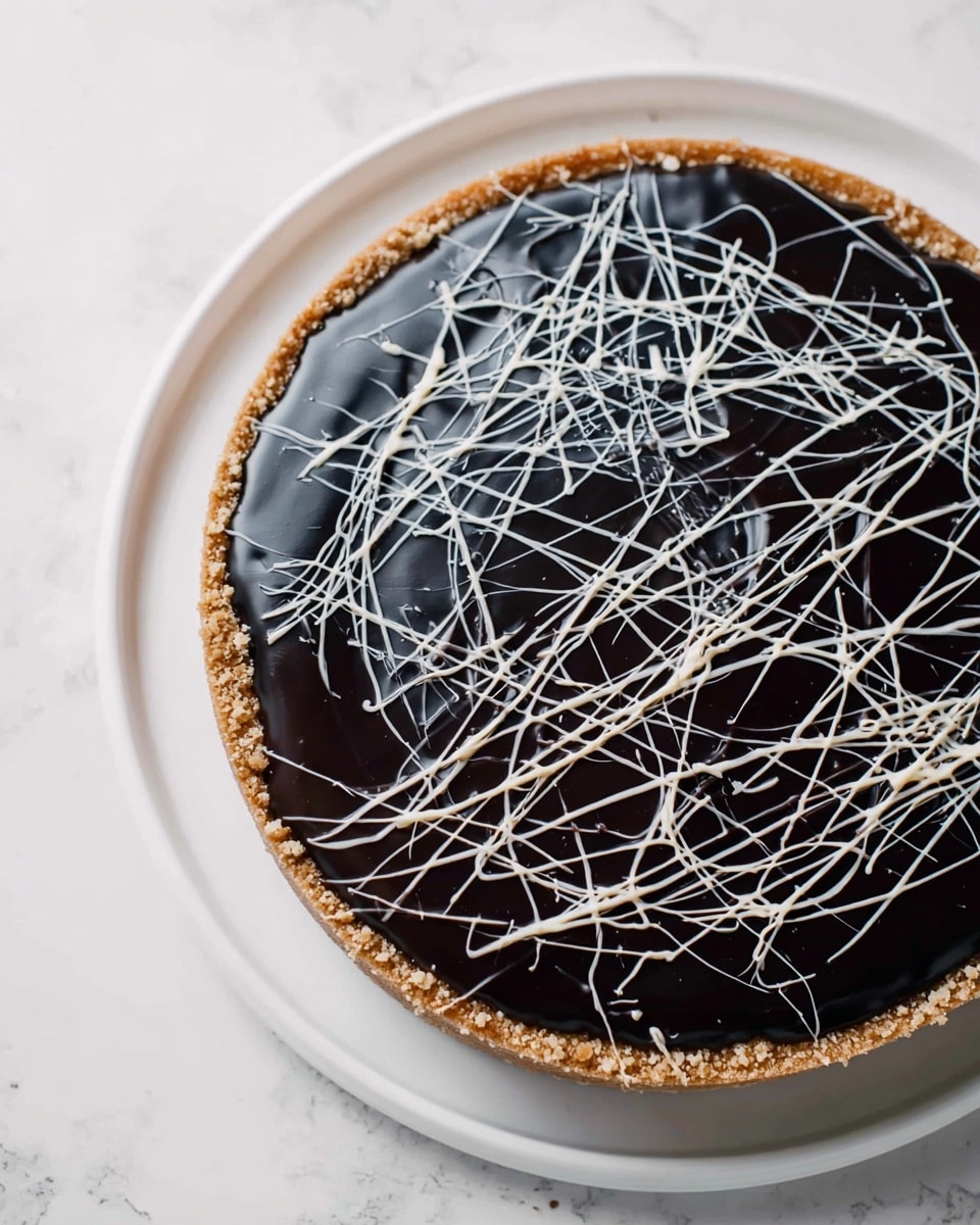 A round dessert with three visible layers sits on a white plate over a white marbled surface. The bottom layer is a crumbly, light brown crust that forms a thick border around the edge. Above that is a smooth, deep black filling that looks shiny and creamy, taking up the main part of the dessert. On top, thin white lines are drizzled randomly, creating a spiderweb or abstract pattern over the black surface, adding texture and contrast. Photo taken with an iphone --ar 4:5 --v 7