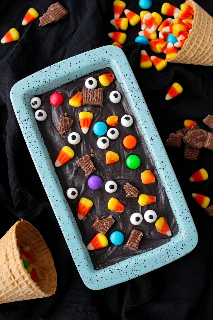 Boo Batter No-Churn Ice Cream with Kit Kats and Halloween Colors, Halloween ice cream recipes, no-churn fall desserts, spooky Halloween dessert ideas, easy Halloween ice cream - A rectangular dish with a light blue speckled container holds a smooth, dark black surface of dessert. On top, there are scattered small white candy eyeballs with black centers, colorful round candy pieces in orange, yellow, green, red, and purple, pieces of candy corn with yellow, orange, and white layers, and broken sections of chocolate wafer candy bars. The scene is against a black fabric background with two waffle cones spilling colorful candy wrappers and candy into the frame. photo taken with an iphone --ar 2:3 --v 7