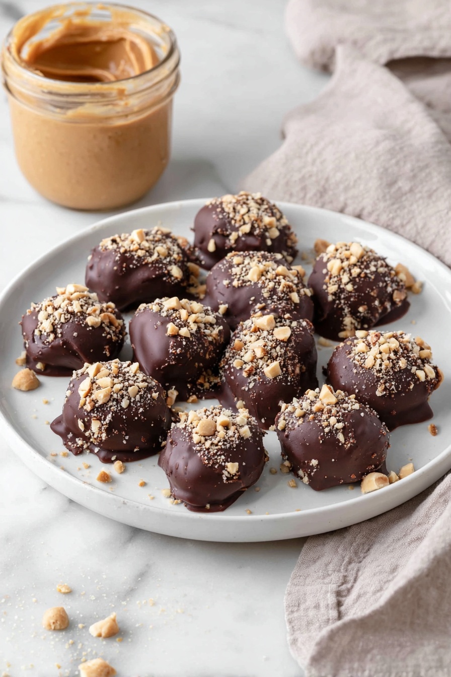 Date Snickers, healthy date snickers, homemade candy bars, no-bake snack, best date snickers recipe - A white plate holds eleven bite-sized treats, each covered in a thick, dark brown chocolate layer with a slightly glossy and smooth texture. On top of each piece, there is a sprinkling of small, light tan chopped nuts adding a rough, crunchy texture. The treats are arranged loosely close to each other in the center of the plate. In the background, there is an open jar filled with smooth, creamy peanut butter in a light brown shade, and a light beige cloth with a soft, woven texture lies nearby on a white marbled surface. Photo taken with an iphone --ar 2:3 --v 7