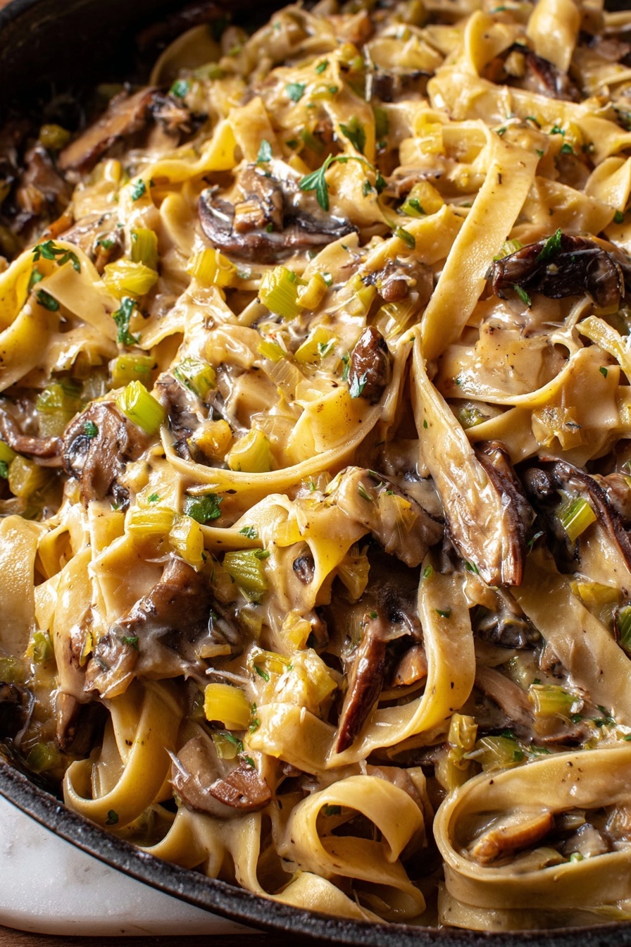 Caramelized Leek & Mushroom Gruyere Pasta, caramelized leek pasta, mushroom and Gruyere pasta, comforting leek pasta recipe, easy mushroom pasta dish - This close-up image shows a pan full of creamy pasta with broad, flat noodles tangled among large, uneven pieces of dark brown mushrooms. The sauce is light beige and coats the pasta and mushrooms, with small diced bits of green and yellow vegetables spread throughout, adding texture and color. The surface below the pan has a white marbled texture visible on the edges. photo taken with an iphone --ar 2:3 --v 7