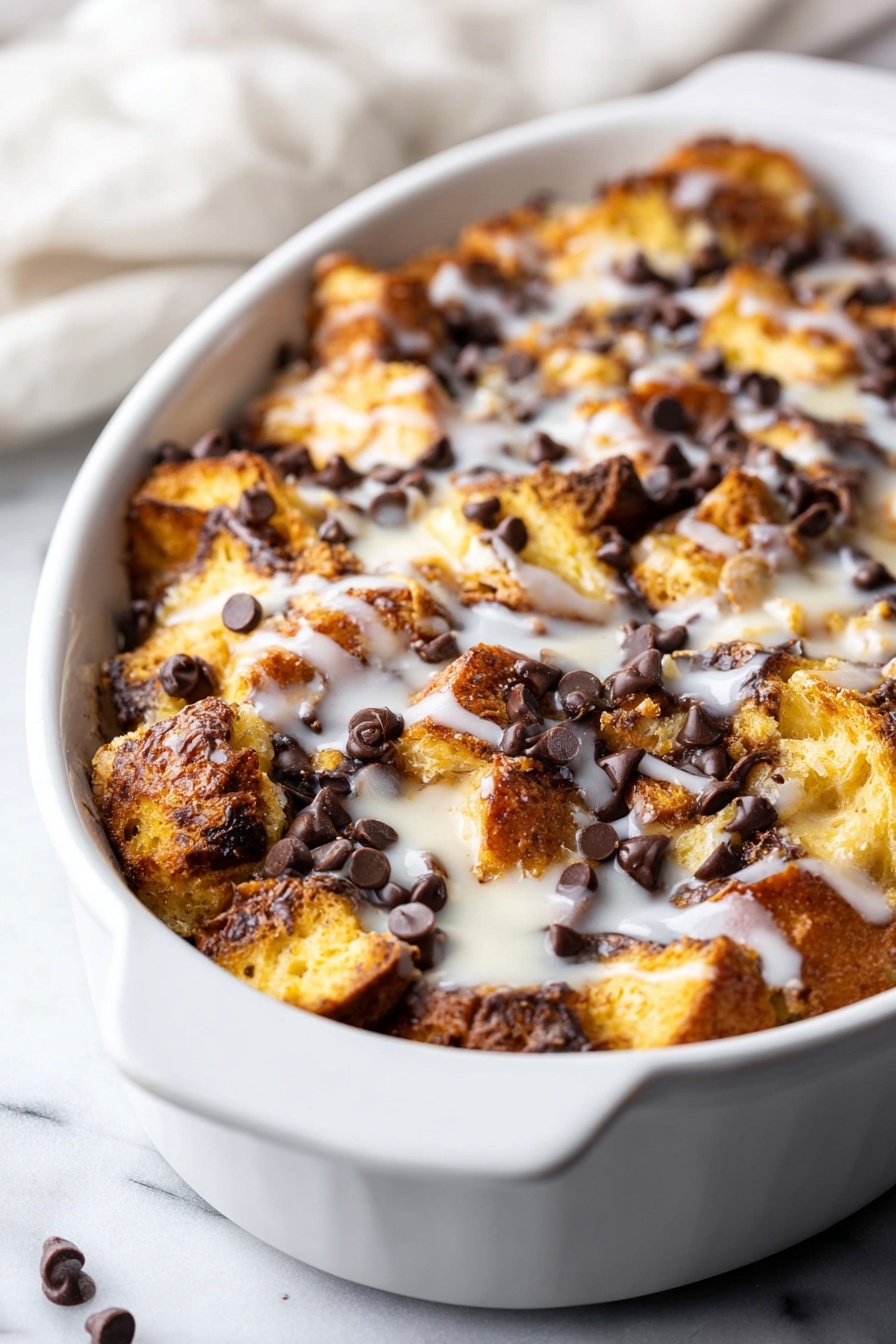 Tres Leches Bread Pudding with Chocolate Chips, Tres Leches Bread Pudding, Chocolate Chip Dessert, Milk-Soaked Bread Pudding, Easy Tres Leches Dessert - A white oval dish holds a baked bread pudding with layers of golden brown, toasted bread pieces that have a slightly crunchy texture, scattered generously with dark chocolate chips that add a rich contrast. The pudding is topped with a light drizzle of white glaze, giving a shiny and smooth finish. The dish sits on a white marbled surface with part of a soft white cloth in the background. photo taken with an iphone --ar 2:3 --v 7