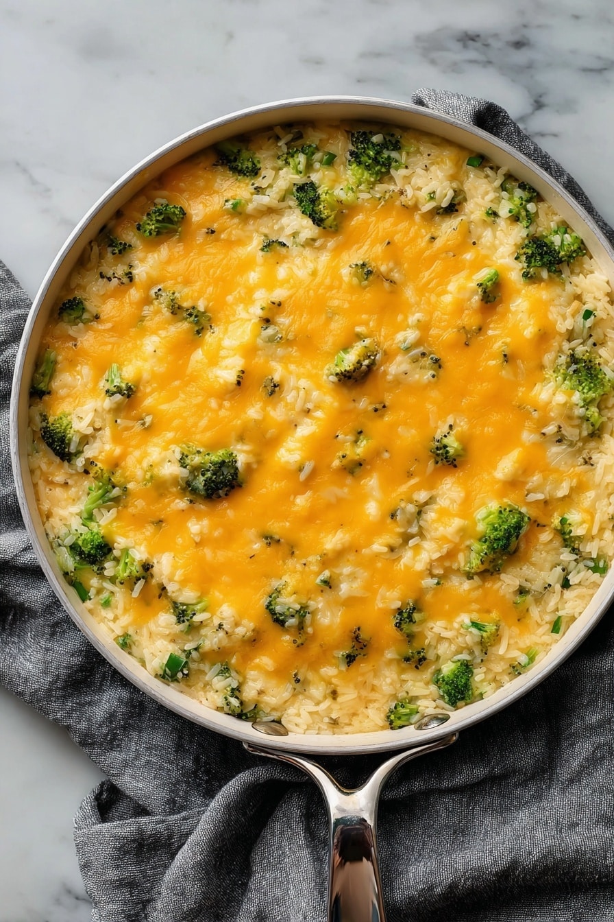 Cheesy Broccoli Rice Vegan Casserole, vegan broccoli casserole, plant-based cheesy rice casserole, healthy vegan broccoli bake, dairy-free cheesy casserole - The dish is served in a round white pan with a silver handle, placed on a gray cloth over a white marbled surface. It has two main layers: the bottom layer is a mix of cooked white rice with small pieces of broccoli, giving a textured base of green and white. The top layer is a smooth, even spread of melted orange cheese covering the rice and broccoli, with small bits of broccoli peeking through. The cheese looks soft and slightly shiny, adding a creamy contrast to the grainy rice below. photo taken with an iphone --ar 2:3 --v 7