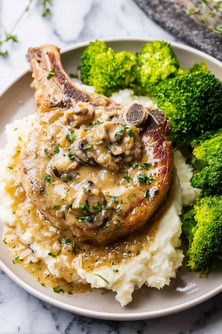 Easy Smothered Pork Chops, tender pork chops with gravy, savory pork chop dinner, cozy comfort food recipes, simple pork chop recipes - A large cooked pork chop sits in the center of a white plate on a bed of creamy mashed potatoes as the bottom layer; the pork chop has a light brown color with a creamy mushroom sauce on top, dotted with pieces of mushrooms and sprinkled with small green herbs; to the right side of the plate, there are bright green steamed broccoli florets with a slightly wet texture; the white mashed potatoes have a soft, slightly lumpy texture, and both the pork chop and sauce have a glossy sheen from the sauce; the plate sits on a white marbled surface; photo taken with an iphone --ar 2:3 --v 7