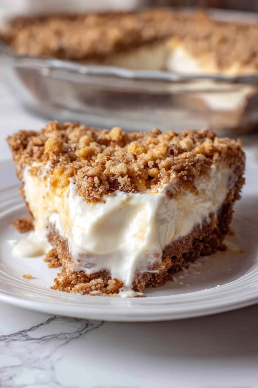 Angel Pecan Pie, light pecan pie, fluffy egg white pecan pie, maple pecan pie, holiday pecan dessert - A close-up of a slice of pie on a white plate with a white marbled surface underneath. The pie has three visible layers: a crumbly brown crust at the bottom, a thick creamy white filling in the middle that is slightly melting and spreading on the plate, and a chunky golden brown crumb topping with some small nut bits on top. In the background, part of a clear glass dish shows the rest of the pie with the same three layers. The photo taken with an iphone --ar 2:3 --v 7