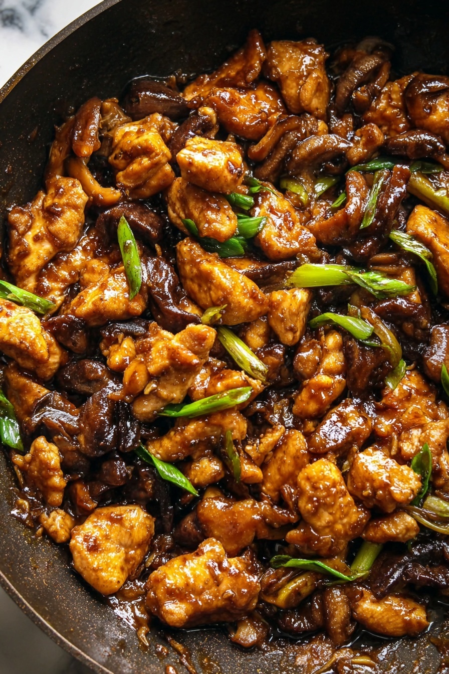 Black Pepper Mushroom Chicken Stir Fry, easy stir fry recipes, healthy chicken stir fry, mushroom chicken dinner, quick Asian stir fry - The image shows a close-up of a dark pan filled with a rich brown stir-fry dish. The stir-fry has several layers of golden brown cooked chicken pieces that look crispy on the edges, mixed with dark brown cooked mushroom slices. Scattered throughout the dish are small pieces of bright green sliced spring onions, adding a fresh contrast. The sauce covering the ingredients is glossy and thick, giving the dish a shiny look. The background is a white marbled texture. photo taken with an iphone --ar 2:3 --v 7
