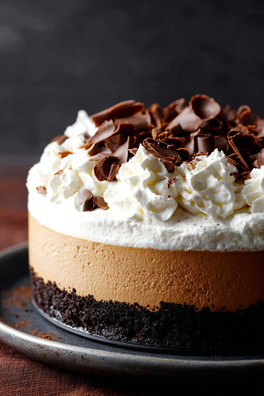 Chocolate Pumpkin Cheesecake with Bourbon Whipped Cream, pumpkin cheesecake with chocolate and bourbon, fall dessert recipes, creamy pumpkin cheesecake, decadent chocolate pumpkin dessert - A three-layer dessert is shown, starting with a dark crumbly chocolate base at the bottom, followed by a thick smooth light brown creamy layer in the middle, topped with a generous fluffy white whipped cream layer. The whipped cream is decorated with scattered dark brown curled chocolate pieces. The dessert sits on a dark surface with a soft dark background. photo taken with an iphone --ar 2:3 --v 7