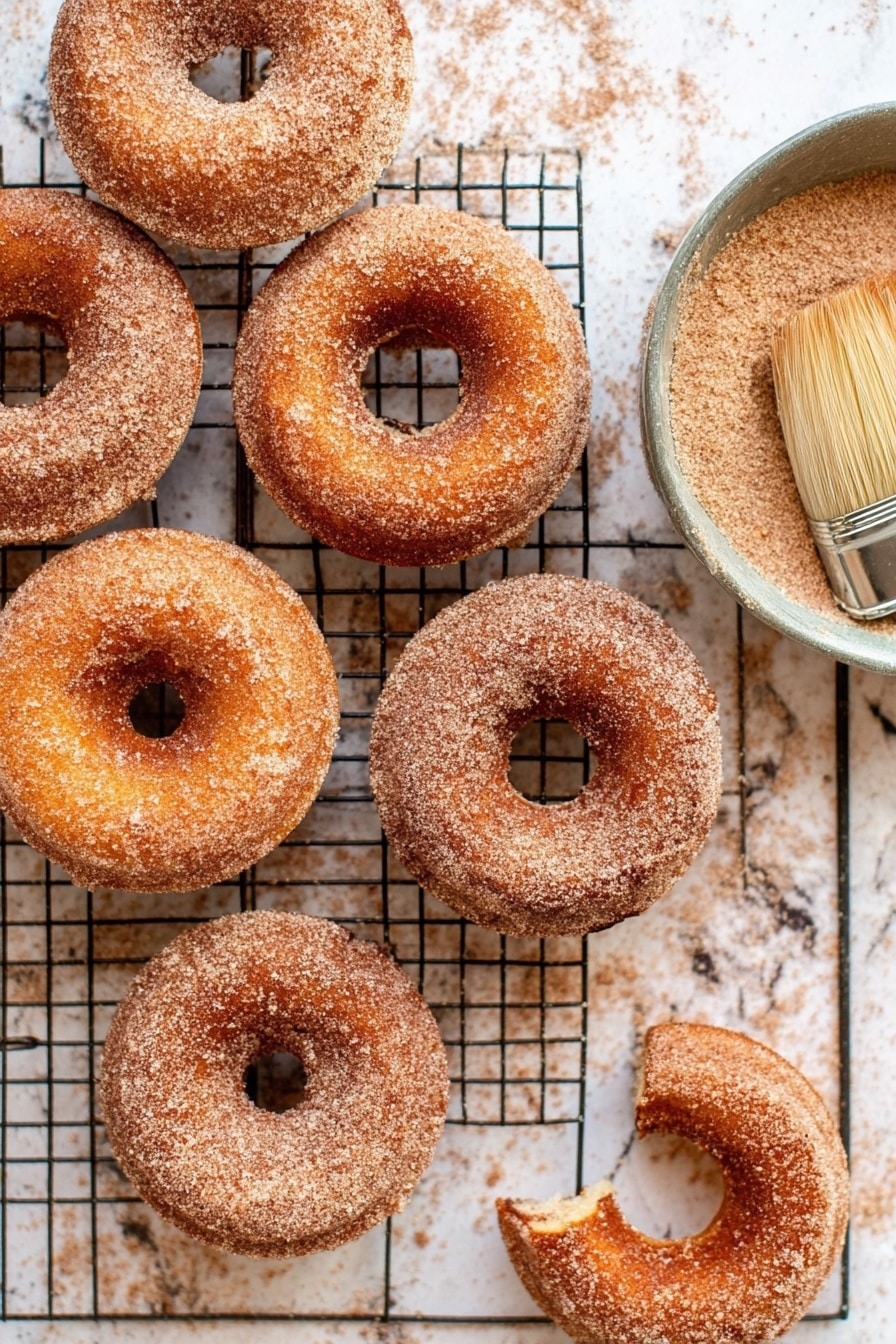 Cinnamon Sugar Doughnuts, homemade cinnamon sugar doughnuts, soft cinnamon doughnuts, easy cinnamon sugar doughnut recipe, best cinnamon doughnuts - Seven cinnamon sugar donuts are arranged loosely on a black wire cooling rack. Each donut has a smooth, light brown surface coated with a fine layer of cinnamon sugar that gives a slightly grainy texture. The donuts have a soft, round shape with a distinct hole in the middle, and their edges are gently rounded. The cooling rack sits on a white marbled surface, which contrasts softly with the warm colors of the donuts. photo taken with an iphone --ar 2:3 --v 7
