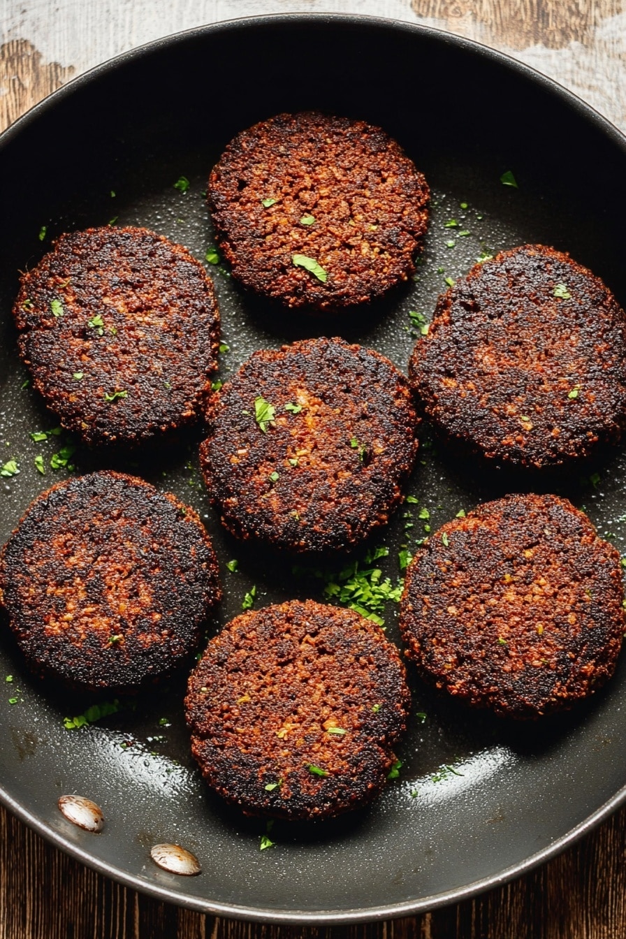 Vegan Breakfast Sausage, plant-based breakfast sausage, vegan sausage recipe, healthy vegan breakfast, vegetarian sausage skillet - The image shows eight dark brown, crispy patties arranged evenly inside a black round pan. The patties have a coarse texture with some small bits visible, and are sprinkled lightly with small green herb pieces. The background surface seen at the top is wooden but will be imagined as a white marbled texture. The pan has a slightly shiny area where the light reflects. photo taken with an iphone --ar 2:3 --v 7
