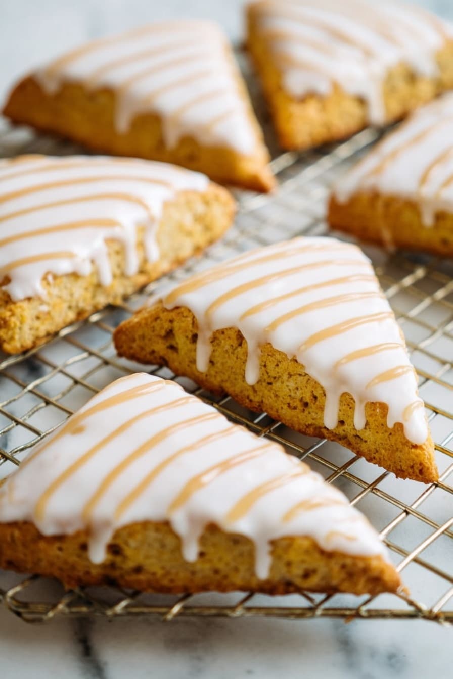 Starbucks Copycat Vegan Pumpkin Scones, vegan pumpkin scones, fall breakfast ideas, dairy-free pumpkin scones, vegan baking recipes - The image shows a close-up of several triangular scones placed on a wire cooling rack over a white marbled surface. Each scone has a golden-brown, slightly rough texture base with a smooth, thick white icing layer covering the top. Over the white icing, there are thin, even lines of light brown drizzle arranged diagonally from one corner to the other. The scones are arranged in a casual pattern, filling the frame with their detailed textures and colorful toppings. photo taken with an iphone --ar 2:3 --v 7