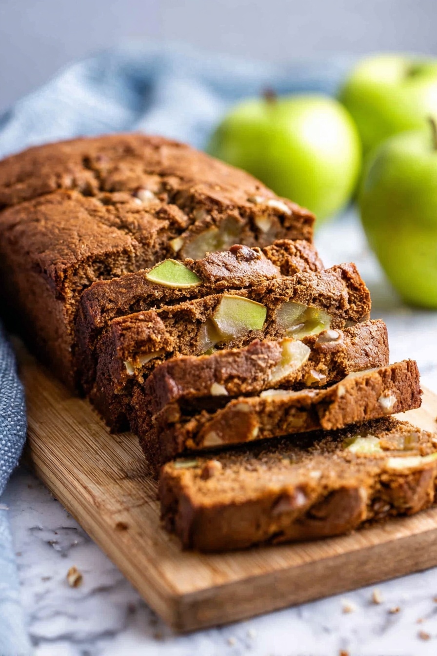 Moist Cinnamon Apple Bread, Cinnamon Apple Bread recipe, easy apple bread, cozy breakfast bread, spiced apple quick bread - A loaf of brown apple bread with a soft, cracked crust sits on a wooden board placed on a white marbled surface. The bread is sliced into thick pieces, revealing a moist inside with chunks of green apple and nuts scattered throughout. The background has a few whole green apples and a light blue kitchen towel, slightly blurred to keep the focus on the bread. photo taken with an iphone --ar 2:3 --v 7