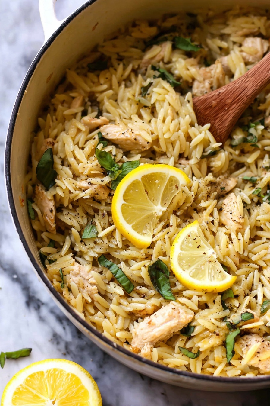 Lemon Chicken and Orzo, lemon chicken skillet, lemon chicken dinner, one-pan chicken and orzo, easy lemon chicken recipe - The image shows a white pot filled with cooked orzo pasta mixed with small pieces of light brown chicken and fresh green basil leaves scattered throughout. Two bright yellow lemon slices rest on top as a garnish, and there are visible specks of black pepper sprinkled across the dish. A wooden spoon stirs the orzo on the right side, and a lemon wedge is blurred in the white marbled background. The texture of the orzo looks soft and slightly shiny, mixing well with the tender chicken pieces. photo taken with an iphone --ar 2:3 --v 7
