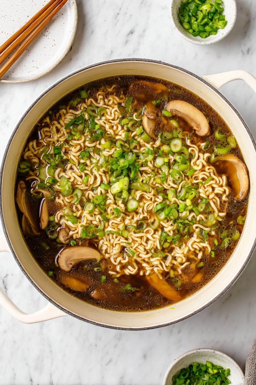 Easy Vegan Ramen, vegan ramen recipe, plant-based ramen, healthy vegan noodle soup, vegetarian ramen bowls - A large white pot filled with dark brown broth containing light beige cooked curly noodles scattered throughout. Several slices of light brown mushrooms float on top, mixed with plenty of bright green chopped scallions spread evenly across the surface. The pot handles are visible on the sides, resting on a white marbled surface. In the background, a round white plate with wooden chopsticks rests towards the top left, and a small white bowl with extra chopped scallions sits on a matching saucer towards the top right. photo taken with an iphone --ar 2:3 --v 7