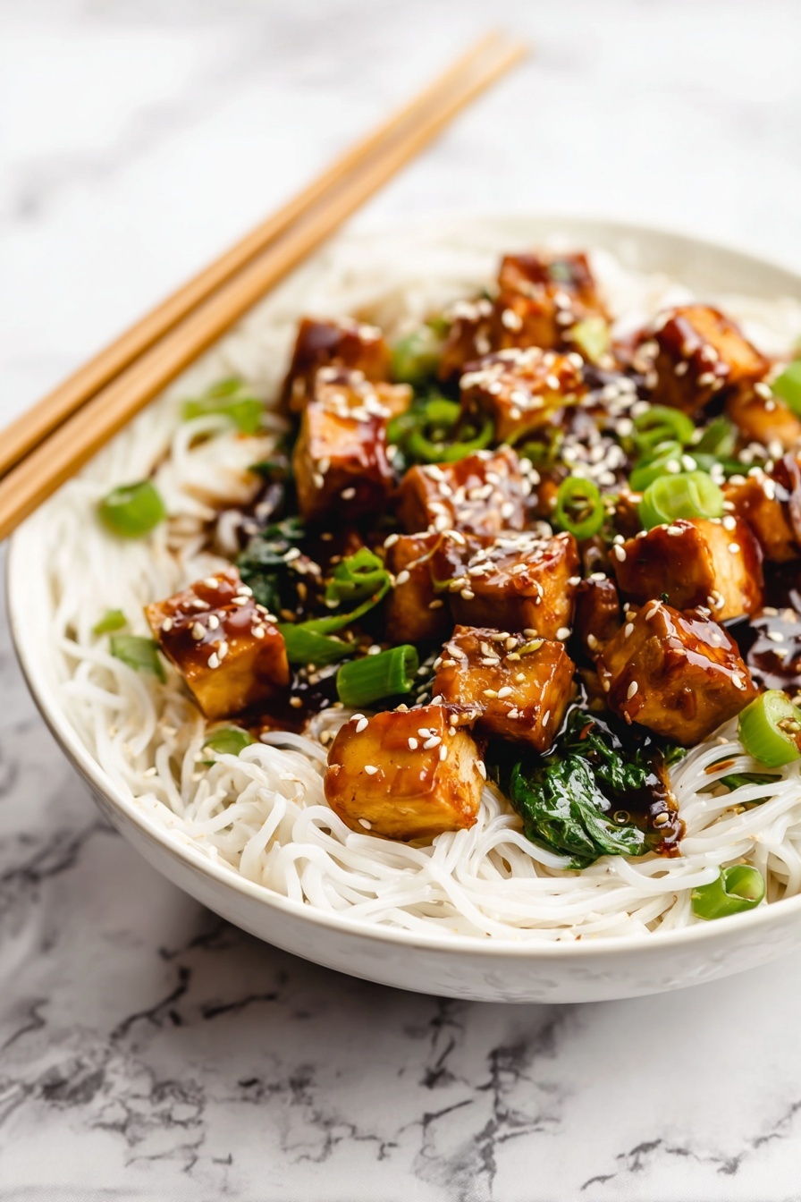 Quick One Pan Tofu Stir Fry, tofu stir fry, easy vegan dinner, quick weeknight meal, healthy tofu recipes - A white bowl is filled with thin white noodles forming the base layer. On top, there are medium-sized golden brown tofu cubes coated in a shiny dark brown sauce. Bright green chopped scallions and spinach leaves are mixed in with the tofu. White sesame seeds are sprinkled over the tofu pieces, adding texture and color contrast. Wooden chopsticks rest on the edge of the bowl over a white marbled surface in the background. Photo taken with an iphone --ar 2:3 --v 7