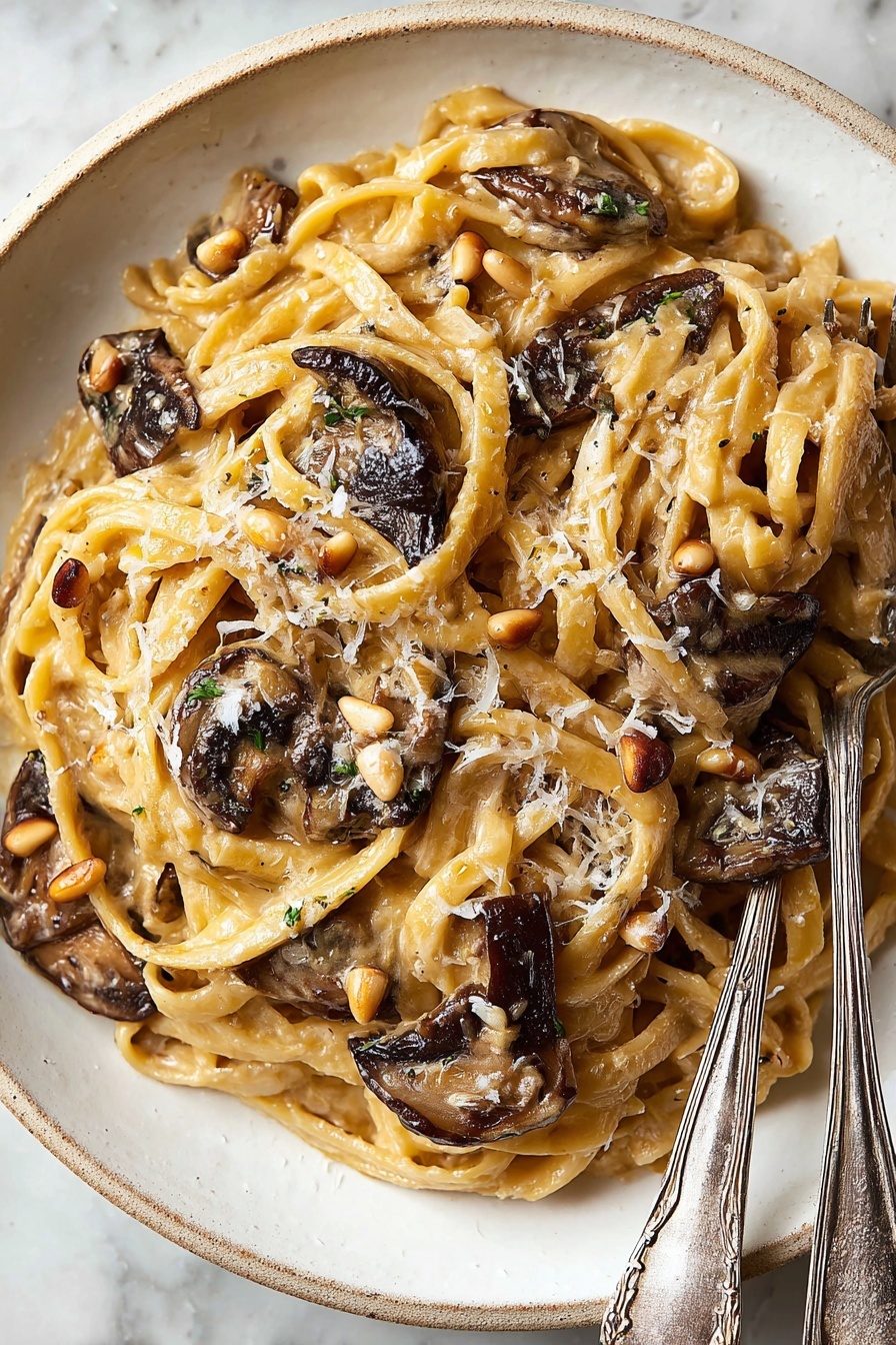 Caramelized Leek & Mushroom Gruyere Pasta, caramelized leek pasta, mushroom and Gruyere pasta, comforting leek pasta recipe, easy mushroom pasta dish - A white plate holds a dish of fettuccine pasta mixed with a creamy light brown sauce. The pasta strands are soft and twisted around each other, topped with several pieces of dark brown, slightly crispy mushrooms scattered on top and inside. Small tan pine nuts and grated pale yellow cheese are sprinkled evenly over the pasta. To the right side of the plate, two silver forks with delicate patterns rest partially on the pasta. The plate sits against a white marbled surface. Photo taken with an iphone --ar 2:3 --v 7