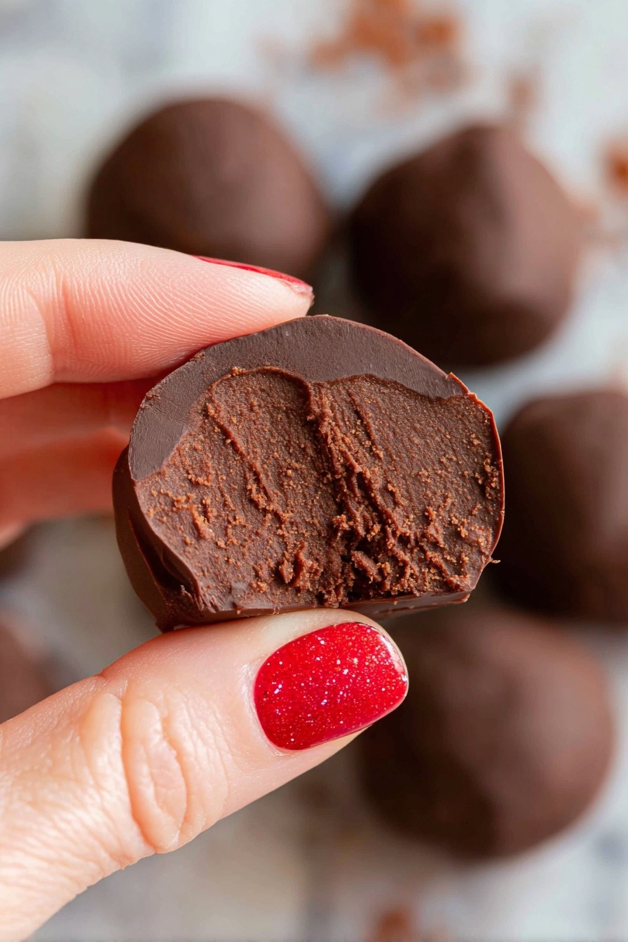 Healthy Black Bean Chocolate Balls, healthy chocolate snack, vegan black bean treats, no-bake healthy desserts, nutritious chocolate bites - A round white bowl filled with several smooth, shiny dark chocolate balls stacked together. Two of the chocolate balls are cut in half and placed on top, revealing a dense, rich, and slightly grainy brown chocolate filling inside. The bowl sits on a white marbled surface, giving a clean and bright look. The chocolate balls have a glossy outer layer with some small wrinkles, showing a contrast between the shiny dark coating and textured inside. Photo taken with an iphone --ar 2:3 --v 7