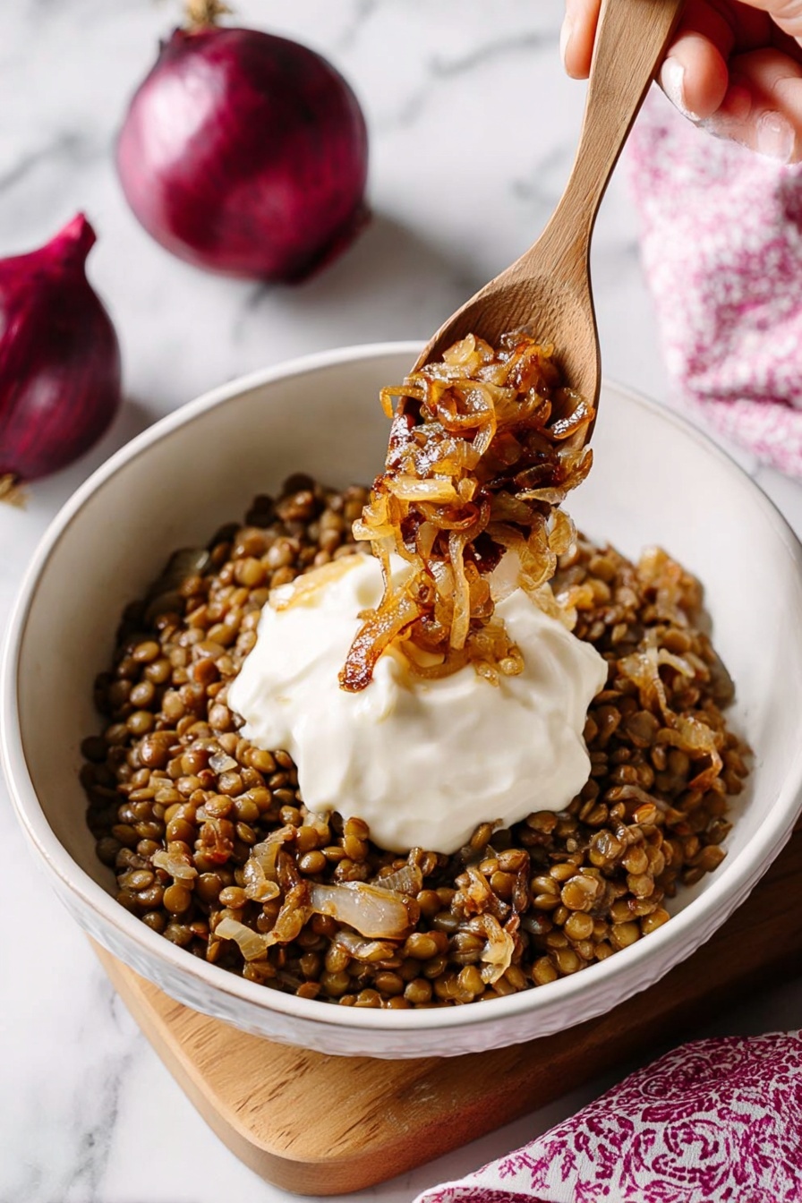 Mujadara Lentil and Rice, Lentil and Rice dish, Middle Eastern Lentil Recipe, Comfort Food with Lentils, Caramelized Onion Lentils - A white bowl filled with a base layer of cooked lentils mixed with small pieces of caramelized onion, creating a brown and slightly textured bed. On top, there is a smooth, thick white dollop of sauce centered in the bowl. A wooden spoon is positioned above the bowl, held by a woman's hand, scooping some golden-brown caramelized onions over the sauce. The background features a white marbled surface with two whole red onions partially visible in the upper right corner and a softly blurred pink patterned cloth in the lower right. photo taken with an iphone --ar 2:3 --v 7
