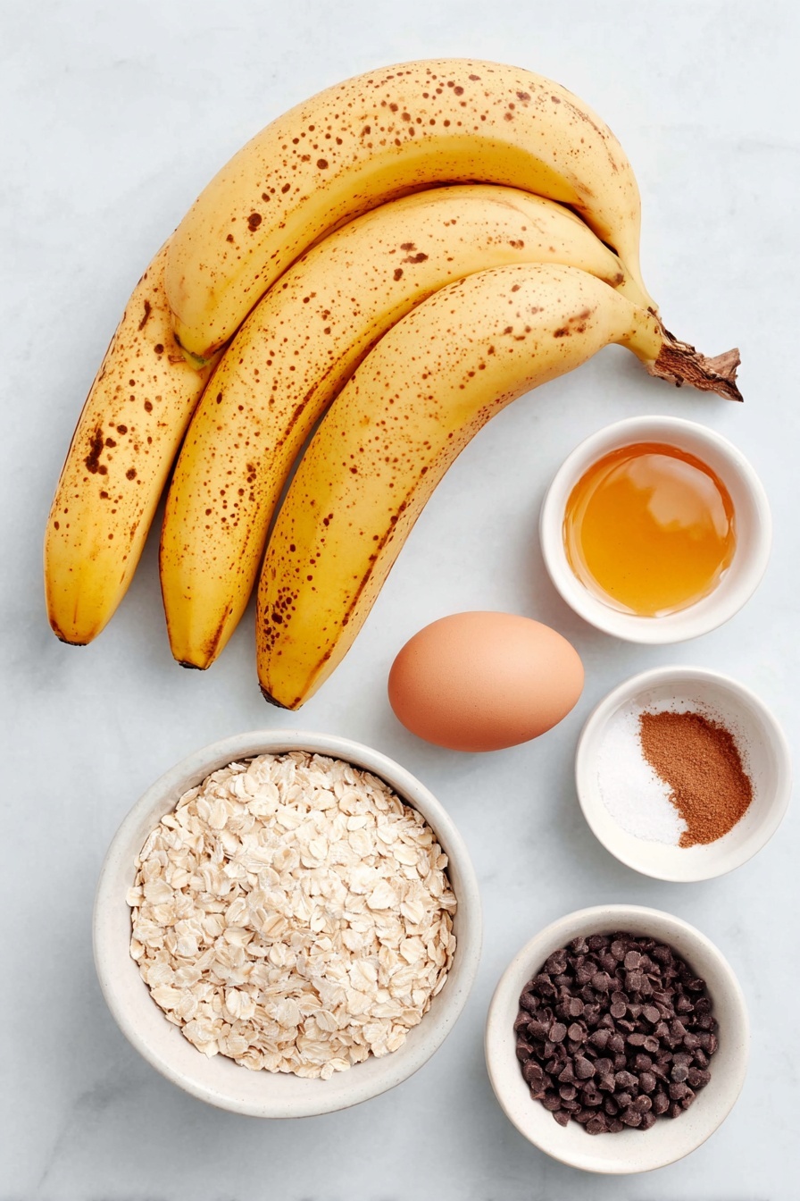 Healthy Banana Oatmeal Cookies, healthy banana cookies, gluten-free oatmeal cookies, easy healthy dessert recipes, wholesome banana snack - Flat lay of three overripe yellow bananas with brown spots, a small white ceramic bowl of golden honey, one whole uncracked brown egg, a small white ceramic bowl filled with quick cooking oats, a small white ceramic bowl containing ground cinnamon powder, a small white ceramic bowl of fine sea salt, and a small white ceramic bowl holding dark chocolate chips, all arranged with perfect symmetry and balanced proportions placed on a clean white marble surface, soft natural light, photo taken with an iPhone, professional food photography style, fresh ingredients, white ceramic bowls, no bottles, no duplicates, no utensils, no packaging --ar 2:3 --v 7 --p awthu7i m7354615311229779997