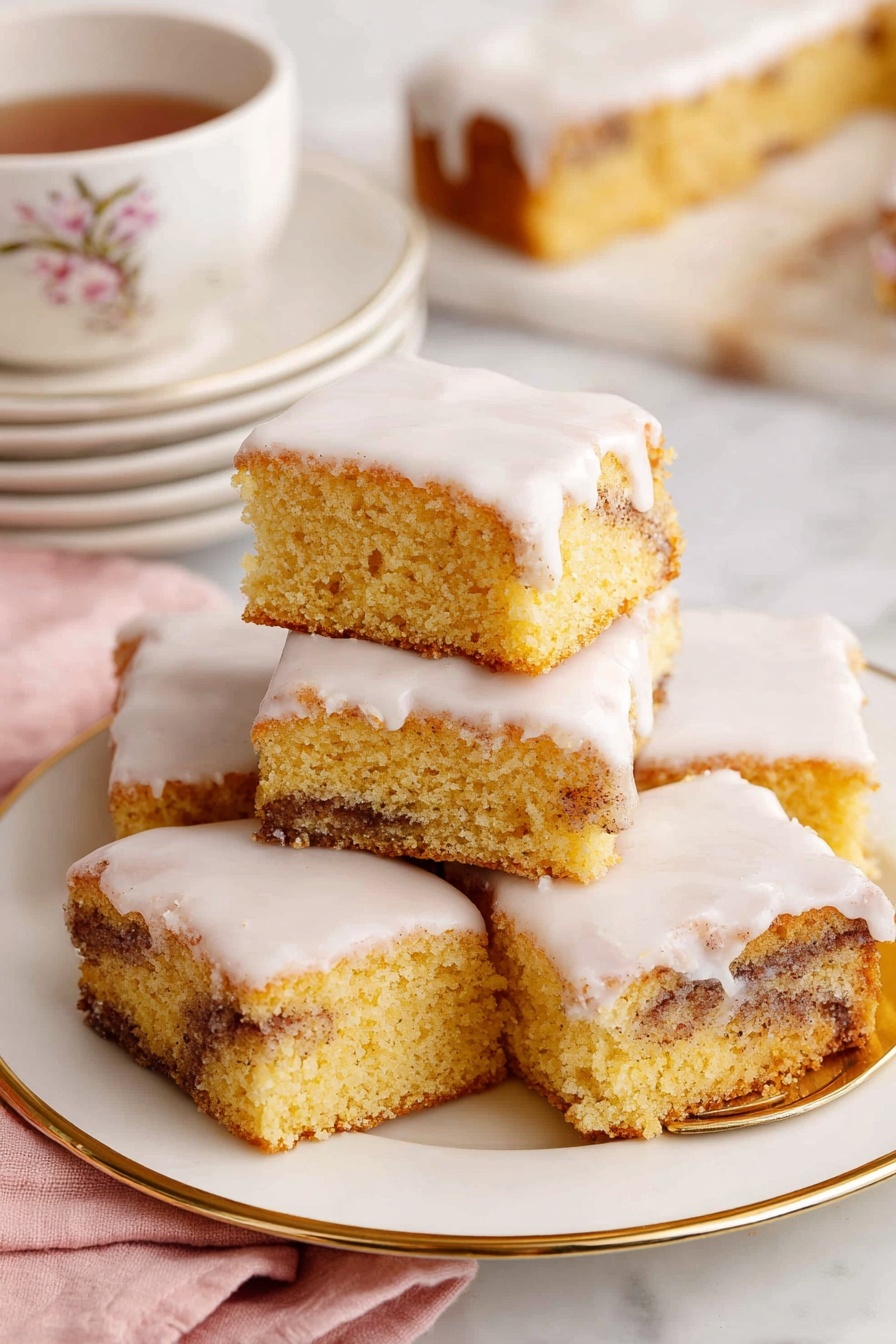 Cinnamon Roll Cake, cinnamon roll cake recipe, easy cinnamon cake, sheet cake cinnamon roll, cinnamon dessert recipe - The image shows a close-up of a square piece of cinnamon roll cake with three layers: a light golden brown cake base with swirls of dark cinnamon running through the middle, topped with a thick, white creamy icing that smoothly covers the top and slightly drips down the sides. The piece sits on a small, white plate with delicate floral and butterfly decorations and a thin gold rim. In the background, there is a white plate with several more pieces of the same cake stacked slightly on top of each other. To the right, a white teacup with a gold rim and small bee design is filled with dark tea. A gold fork lies on a soft pink cloth to the side, and all items rest on a white marbled textured surface. photo taken with an iphone --ar 2:3 --v 7