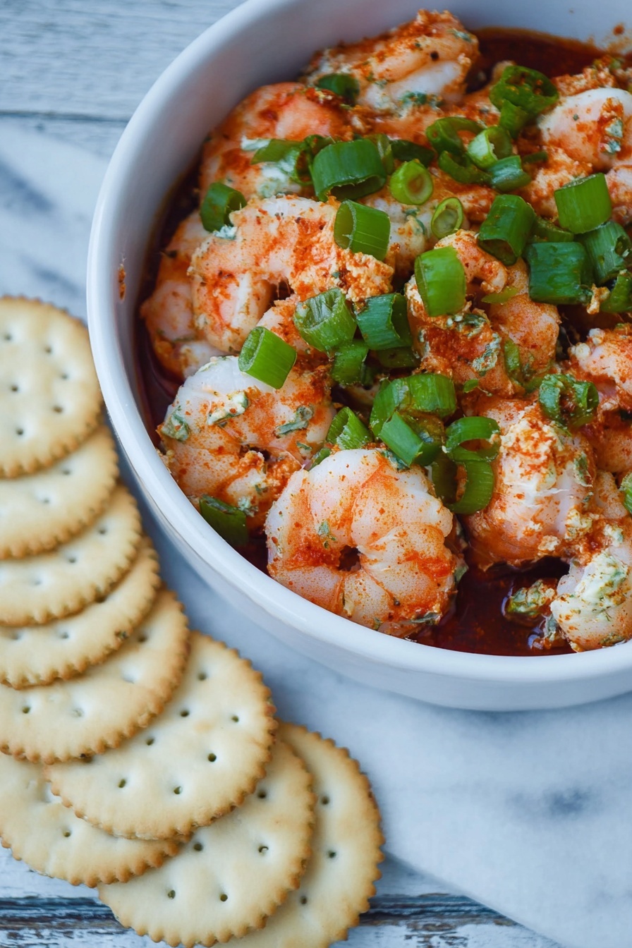 Shrimp Cocktail Dip, Shrimp Dip Recipe, Easy Shrimp Appetizer, Party Dip Ideas, Seafood Dip - The dish shows one white bowl filled with three visible layers: a bottom layer of dark red sauce, a middle layer of pink and white cooked shrimp coated lightly in red spices, and a top layer of bright green chopped scallions scattered evenly over the shrimp. The textures include soft, plump shrimp with some seasoning powder visible and fresh, crisp scallions. The bowl is on a surface of white marbled texture, next to a semi-circle of pale golden round crackers arranged closely in front of the bowl. photo taken with an iphone --ar 2:3 --v 7