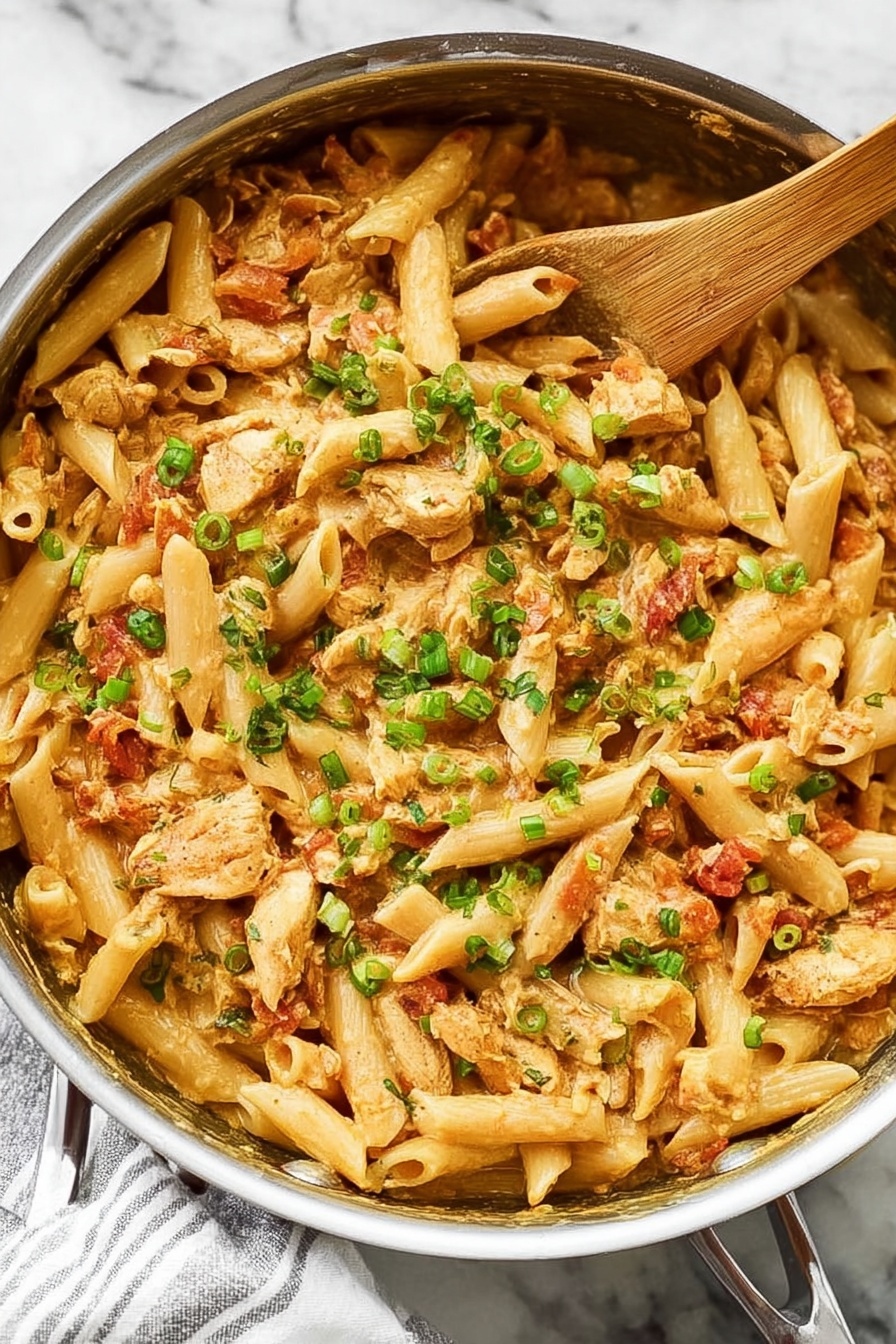 Creamy Cajun Chicken Pasta, Cajun pasta with chicken, quick creamy pasta, spicy chicken pasta, easy one-pot Cajun dish - A close-up view of a large silver pan filled with creamy pasta made with short tube-shaped noodles, chopped light brown cooked chicken pieces, and a rich tan-colored sauce. Mixed in are small bits of red tomatoes and sprinkled chopped green onions on top to add bright green color contrast. A light wooden spoon rests inside the pan on the right side, partially covered by the pasta. The pan is placed on a white marbled surface with a white and gray striped cloth beneath the handle. The dish looks warm and inviting with a mix of soft textures and fresh garnish. Photo taken with an iphone --ar 2:3 --v 7