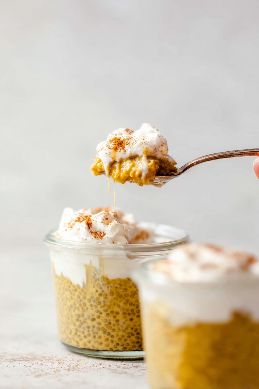 Pumpkin Chia Seed Pudding, healthy pumpkin pudding, fall dessert recipes, vegan chia pudding, cozy pumpkin snack - The image shows a spoon holding a small scoop of a layered dessert with two clear glass jars filled with the same dessert in the background. The bottom layer in the jars is a yellowish-brown pudding with visible chia seeds, giving it a slightly bumpy texture. On top of the pudding is a thick, white cream layer lightly dusted with a brown spice, likely cinnamon. One jar has a woman’s hand partly visible holding a spoon covered with the white cream layer and some pudding drips on the rim. The background and surface are smooth with a white marbled texture. photo taken with an iphone --ar 2:3 --v 7