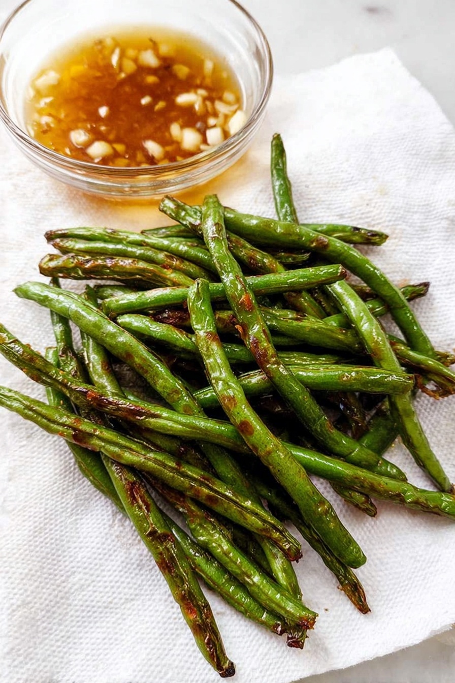 Garlic Green Beans Stir Fry, green beans stir fry, healthy vegetable recipes, quick garlic green beans, savory green bean side dish - A close-up of cooked green beans piled loosely on a white plate, with each bean showing a shiny, slightly wrinkled green surface and some small pieces of browned garlic sprinkled on and around them. The beans have a mix of bright green and darker areas from cooking, and some beans are curved while others lay straight, creating a natural, uneven texture. The background is a white marbled texture. photo taken with an iphone --ar 2:3 --v 7