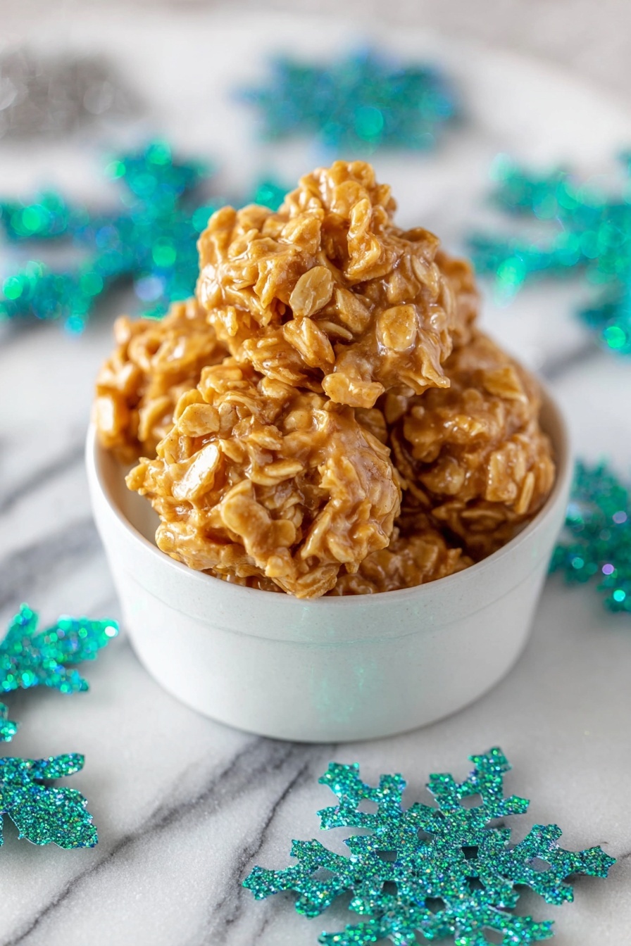 Peanut Butter Cornflake Candy, Cornflake Candy Recipes, No-Bake Candy, Easy Peanut Butter Snacks, Crunchy Confection Recipes - A white bowl decorated with green pine tree patterns and white dots holds five round clusters of a golden-orange snack with a sticky, shiny texture and small visible flakes in each cluster. The bowl is placed on a white marbled surface scattered with large, glittery turquoise and teal snowflake shapes. The clusters look thick and uneven with rough edges. Photo taken with an iphone --ar 2:3 --v 7