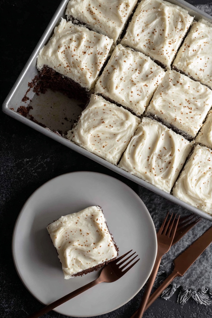 Dark Chocolate Espresso Cake with Brown Butter Frosting, decadent chocolate cake, espresso dessert, homemade chocolate layer cake, rich brown butter frosting - A rectangular metal pan holds a cake cut into nine square pieces, with one piece missing near the center showing a dark, moist chocolate layer under a thick, creamy white frosting. Each frosting layer is spread thick and smooth with slight swirling patterns and small brown specks sprinkled over the top. On a white plate below, one square piece of the cake sits with the same thick white frosting on top and dark chocolate cake layer visible on the sides. Two brown forks lie near the plate on a black textured surface. photo taken with an iphone --ar 2:3 --v 7