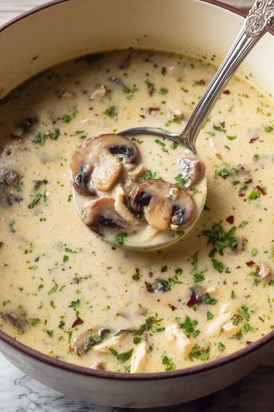 Creamy Chicken Mushroom Soup, hearty chicken mushroom soup, easy homemade soup, comforting mushroom soup, quick creamy chicken soup - A close-up view of a light creamy soup filled with sliced mushrooms and small pieces of chicken, sprinkled with chopped green herbs and tiny dried herbs throughout. The soup has a smooth texture with floating bits of green and brown, and a silver ladle scoops a portion showing three layers of sliced mushrooms, chicken bits, and the creamy broth all mixed. The soup is in a deep white bowl, resting on a white marbled surface. Photo taken with an iphone --ar 2:3 --v 7