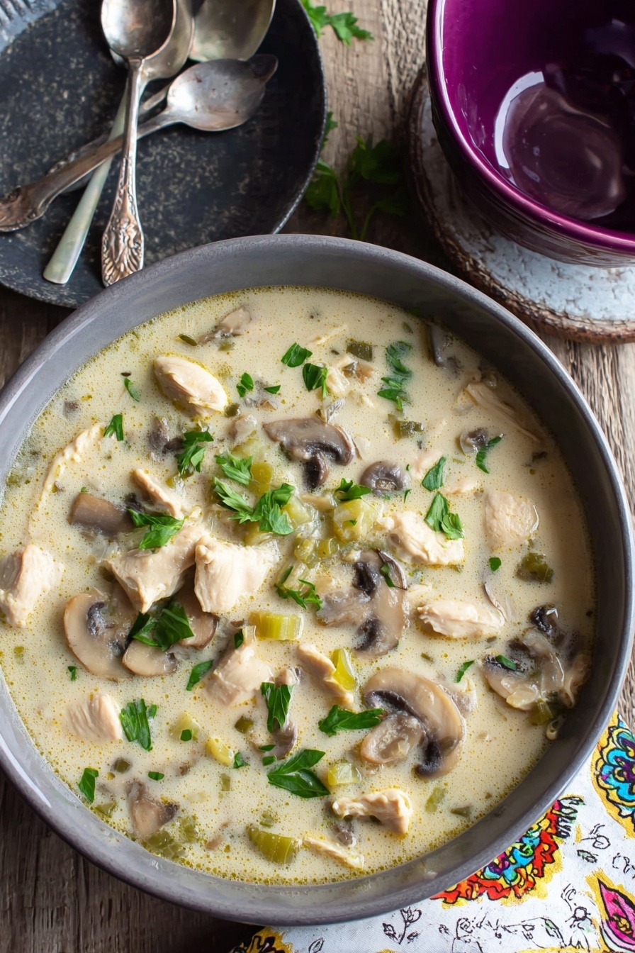 Creamy Chicken Mushroom Soup, hearty chicken mushroom soup, easy homemade soup, comforting mushroom soup, quick creamy chicken soup - A gray bowl filled with creamy soup that has chunks of light beige cooked chicken, sliced brown and white mushrooms, and small pieces of green celery, all mixed in a pale, creamy broth with green parsley leaves scattered on top, sitting on a wooden table next to a dark gray plate with two silver spoons and a purple bowl, with a white napkin that has colorful patterns to the side, the surface beneath is a white marbled texture photo taken with an iphone --ar 2:3 --v 7