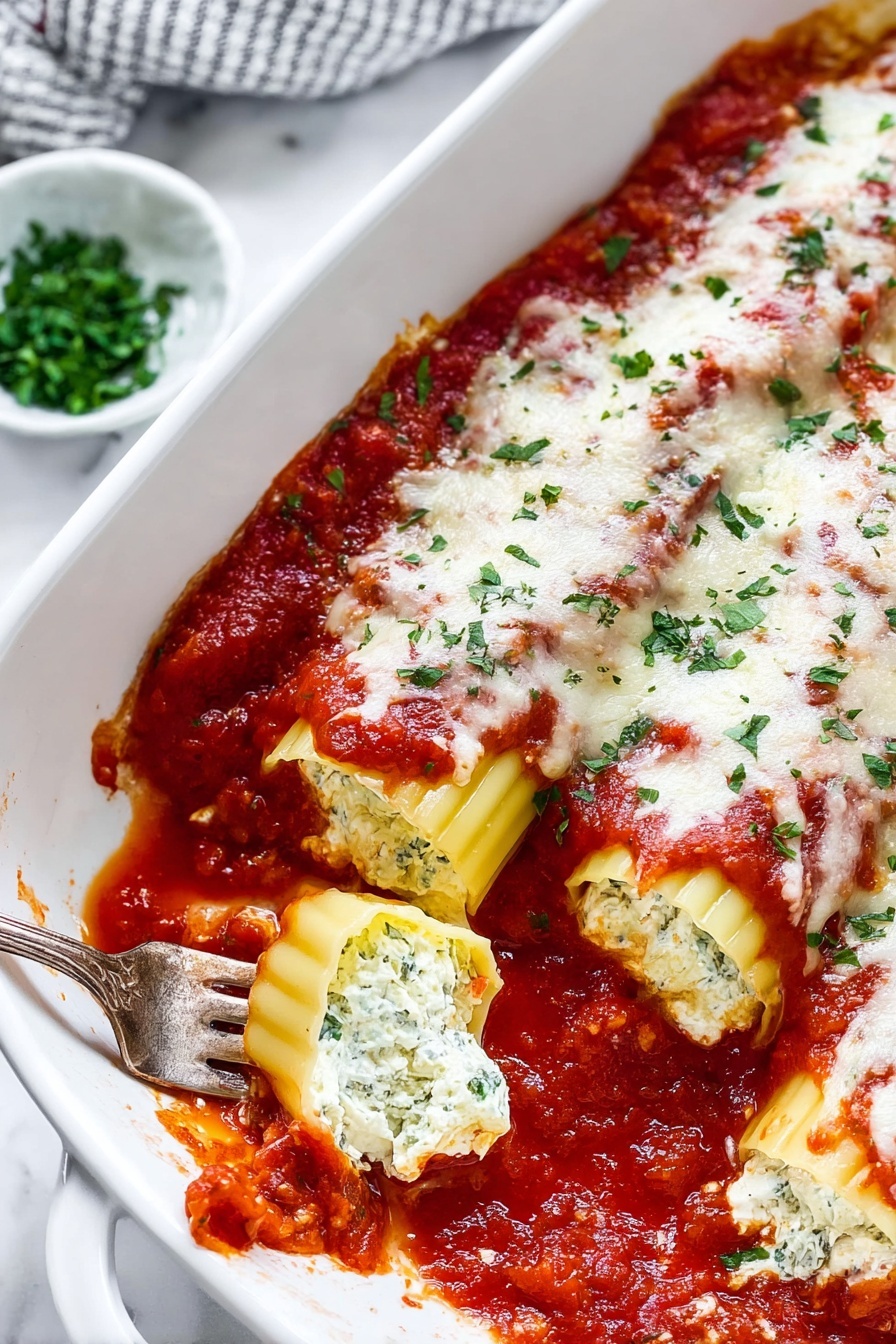 Easy Manicotti with Ricotta and Tomato Sauce, cheesy manicotti dish, homemade Italian manicotti, simple baked pasta recipes, crowd-pleasing Italian dinners - The image shows a white rectangular baking dish filled with two rows of stuffed pasta shells, each covered with a layer of chunky red tomato sauce, melted white cheese, and sprinkled with fresh green herbs. The pasta shells are a pale yellow color with ridged edges visible beneath the sauce and cheese. Around the dish, on a white marbled surface, there are small bowls with green herbs and grated cheese, and some fresh red tomatoes on the vine. The overall look is warm and freshly baked with slight sauce splatters on the edge of the dish, photo taken with an iphone --ar 2:3 --v 7