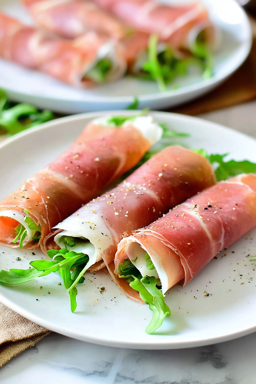 Fig and Prosciutto Roll-Ups, fig and prosciutto appetizer, prosciutto wrapped figs, easy savory appetizers, elegant cheese and fruit bites - Three thin rolled slices of pink prosciutto are placed on a white plate, each filled with green arugula leaves peeking out from one end. The prosciutto has a smooth, slightly shiny texture with light white fat streaks and is lightly sprinkled with coarse black pepper. The white plate sits on a white marbled surface with some leafy greens scattered around its edge. In the background, another white plate holds more similar prosciutto rolls, blurred to focus on the front plate. Photo taken with an iphone --ar 2:3 --v 7