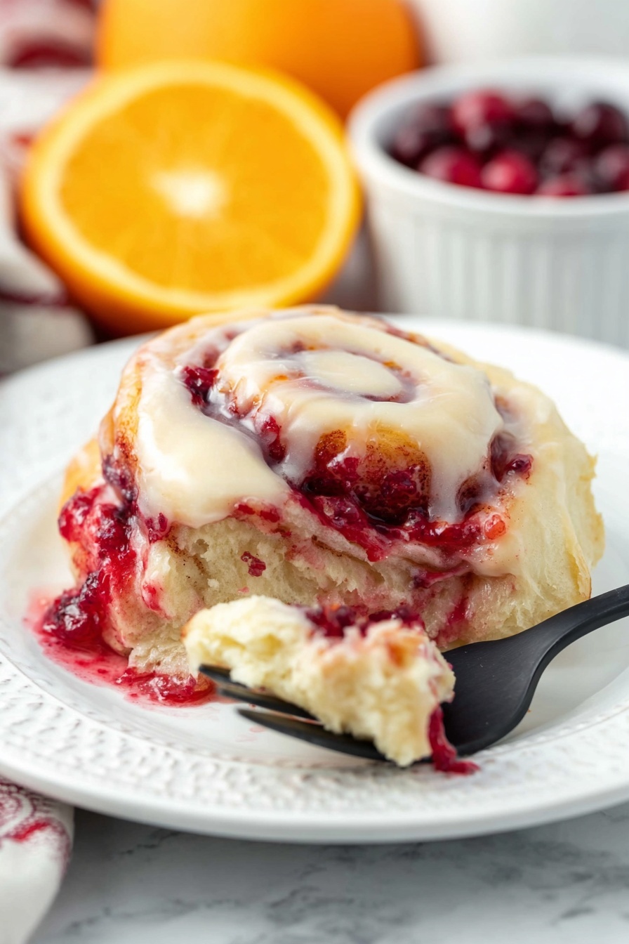Cranberry Orange Sweet Rolls, cranberry orange breakfast ideas, citrus cranberry breakfast treats, holiday sweet roll recipes, easy sweet roll recipes - The dish shows a soft, swirled roll with three main layers: a creamy white icing layer on top that looks smooth and rich, a middle layer with a light beige dough, and a bright red layer of berry filling that appears juicy and slightly thick, seeping out from the roll. The roll is on a white plate with gentle embossed patterns, against a white marbled background. In the front, a black fork holds a small piece of the roll with some berry filling and dough, and in the back, blurred slices of orange and a white bowl filled with deep red cherries add color contrast. Photo taken with an iphone --ar 2:3 --v 7