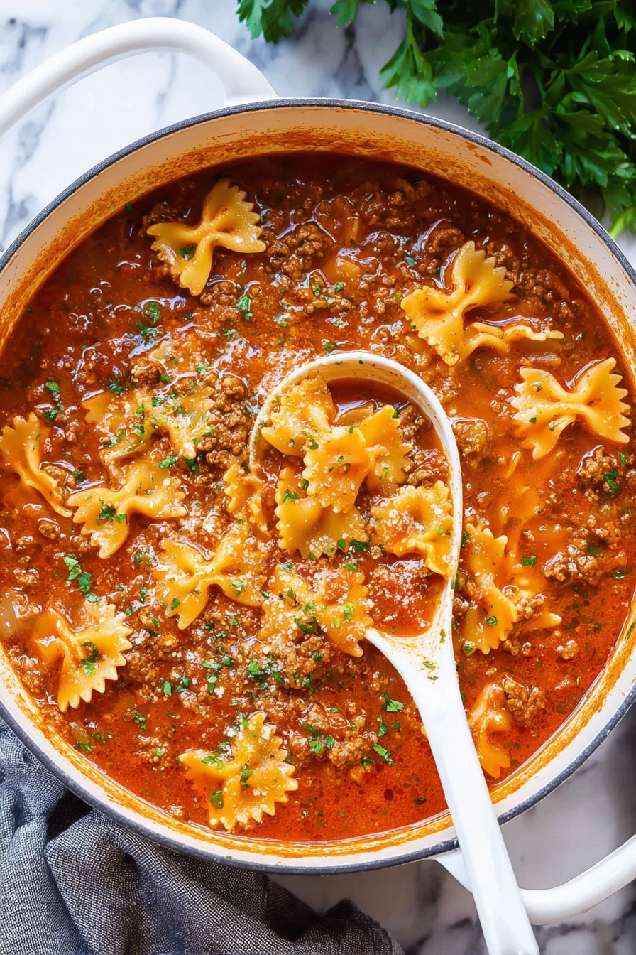 Lasagna Soup, Lasagna Soup with Pasta and Cheese, Easy Lasagna Soup Recipe, Hearty Lasagna Soup, cheesy Italian soup - A large white pot filled with a rich, thick soup showing three main layers: a red tomato broth with a slightly oily surface, small chunks of brown cooked meat spread throughout, and pale orange bow-tie shaped pasta floating on top, sprinkled with small pieces of chopped green herbs. A white spoon is partly dipped in the soup revealing the sauce's thickness and layered textures. The pot is placed on a white marbled surface with some green herbs in the background and a gray cloth to the side, photo taken with an iphone --ar 2:3 --v 7