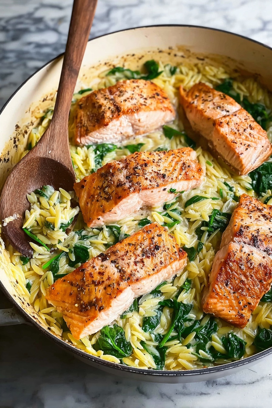 Lemon Herb Salmon with One Skillet Orzo, healthy salmon dinner, easy one-pan seafood recipe, flavorful salmon recipes, quick weeknight salmon - A white pan holds a dish with four pieces of cooked salmon in the center. The salmon is a light orange color with a browned, slightly peppered top layer. Around the salmon, there is a layer of yellow orzo pasta mixed with bright green spinach leaves. The pasta looks soft and slightly shiny, and the spinach leaves are wilted but still colorful. A wooden spoon with some pasta and spinach is resting on the left edge of the pan. The pan sits on a white marbled surface. photo taken with an iphone --ar 2:3 --v 7