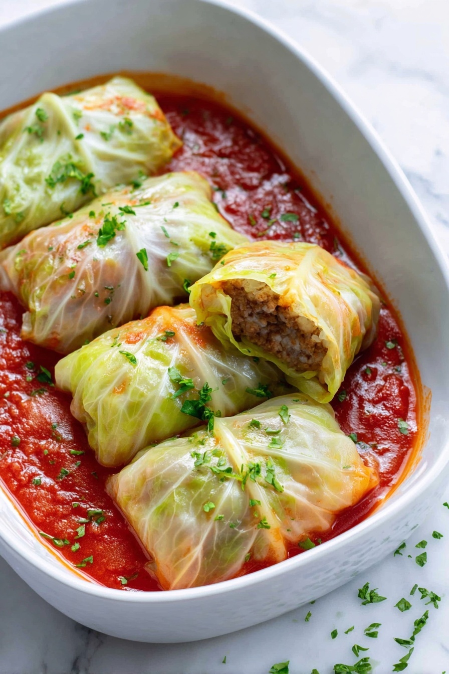 Best Traditional Stuffed Cabbage Rolls, stuffed cabbage rolls recipe, classic cabbage rolls, homemade cabbage rolls, savory stuffed cabbage - The image shows a white baking dish filled with ten cabbage rolls arranged neatly in two rows. Each cabbage roll is wrapped in pale green cabbage leaves that look soft and slightly glossy, with some light browning on edges. The cabbage rolls sit in a rich red tomato sauce that covers the bottom and comes up around the rolls. Small sprinkles of chopped green herbs are scattered over the rolls and sauce, adding color contrast. The dish is set on a white marbled surface with a white and blue striped cloth nearby and some green cabbage leaves partially visible in the background. photo taken with an iphone --ar 2:3 --v 7